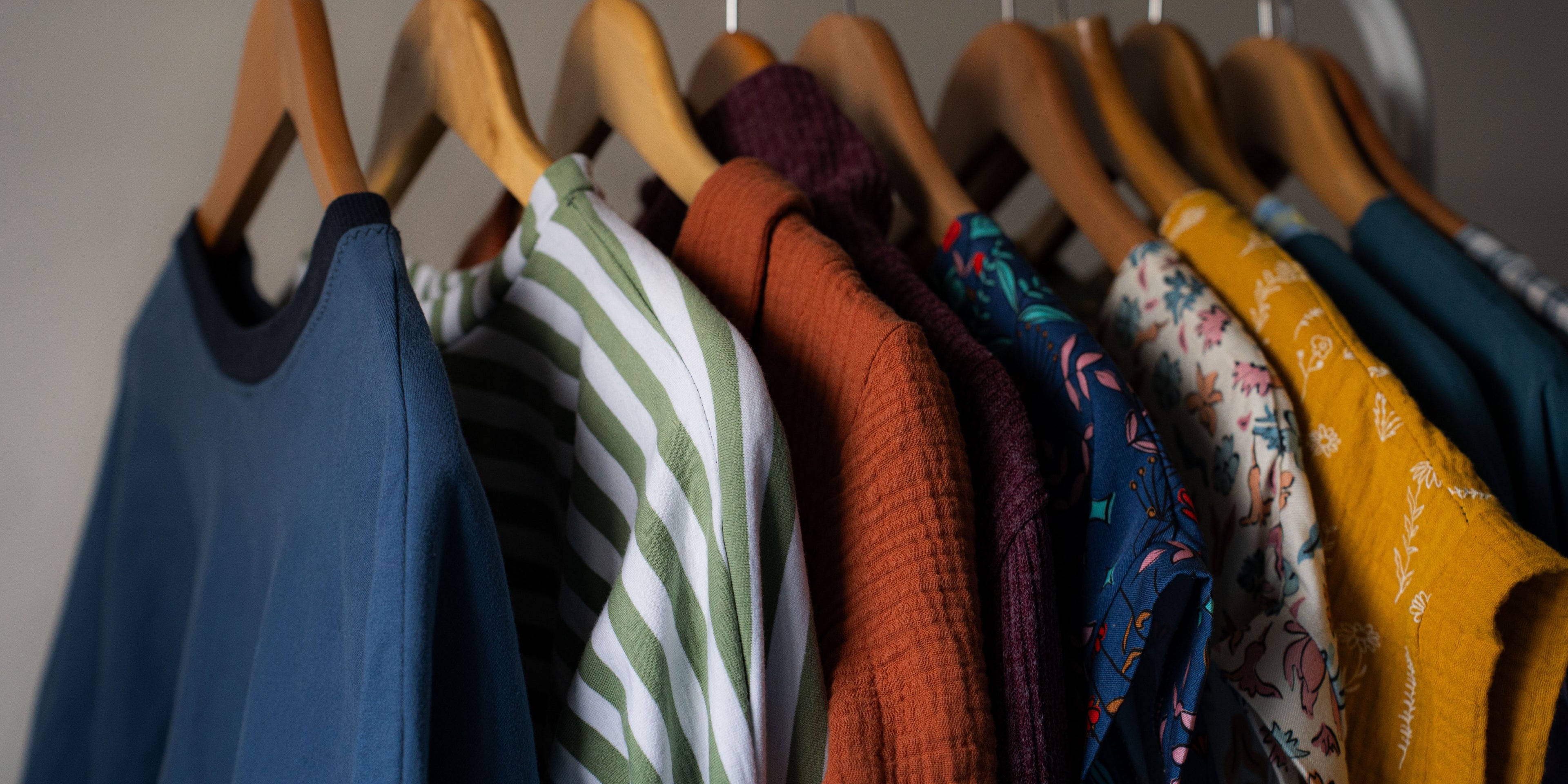 Row of colourful sample clothing hanging on a rail, against neutral background