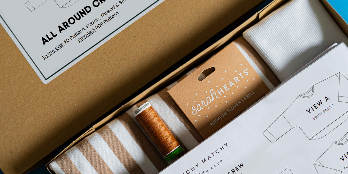 Crafting kit with spools of thread, fabric, and pattern paper in a cardboard box.