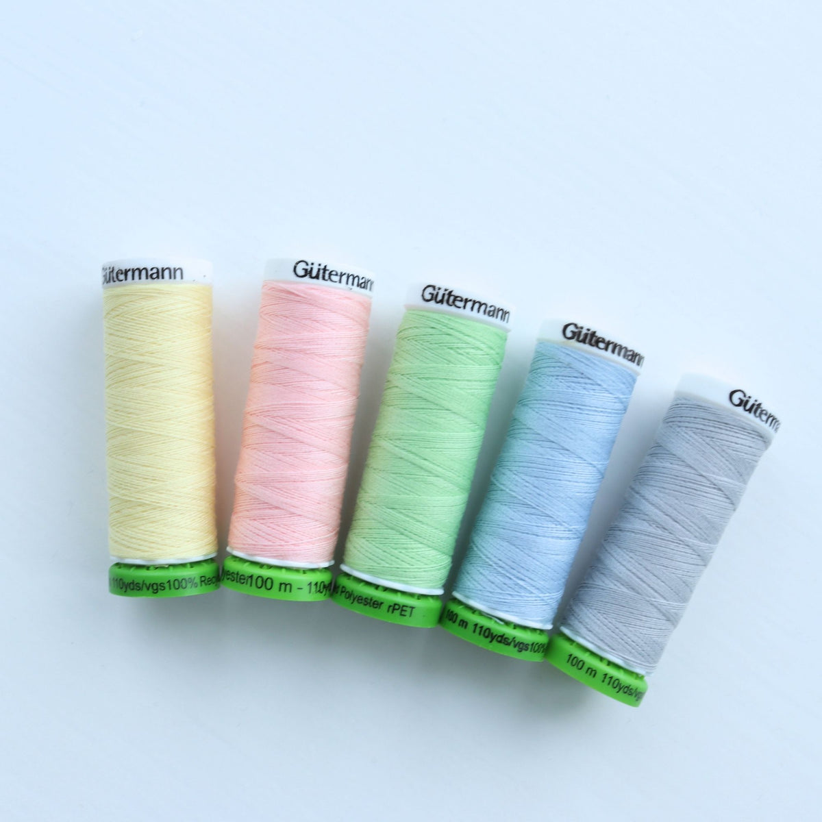 Five Gutermann thread spools in pastel colors on a light blue background