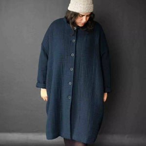 Person wearing a long dark blue coat against a gray background