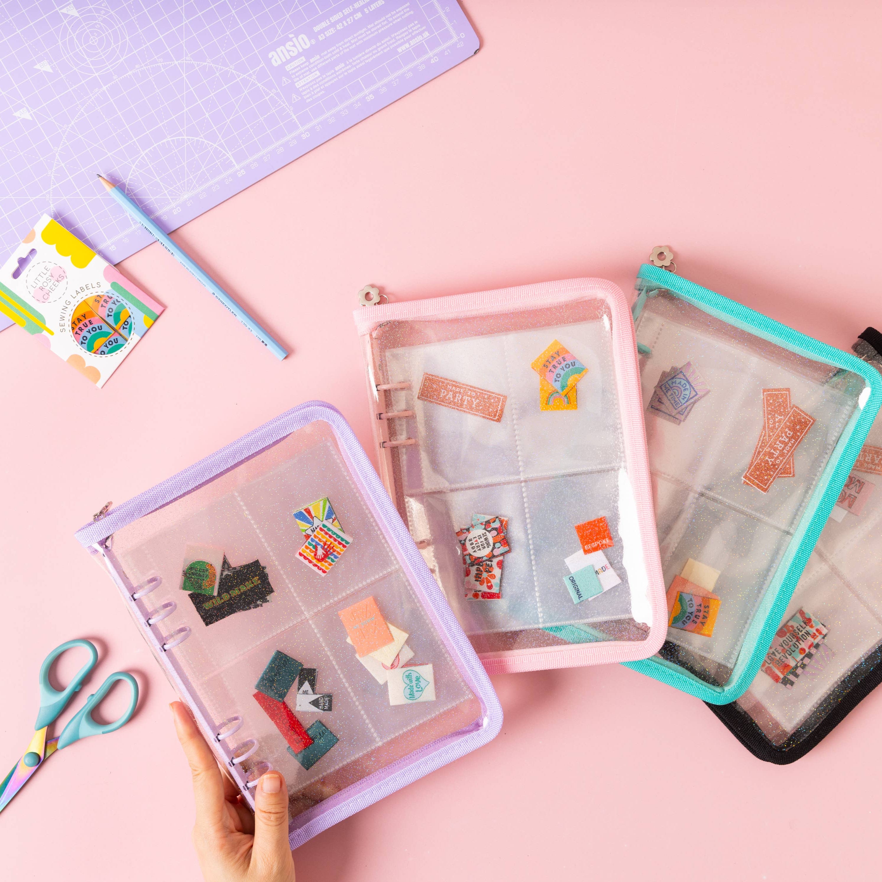 A range of colourful woven sew in label stash folders laid out on the table. Sewing labels are stashed inside the wallets, with scissors a cutting mat and packet of sewing labels on the side.
