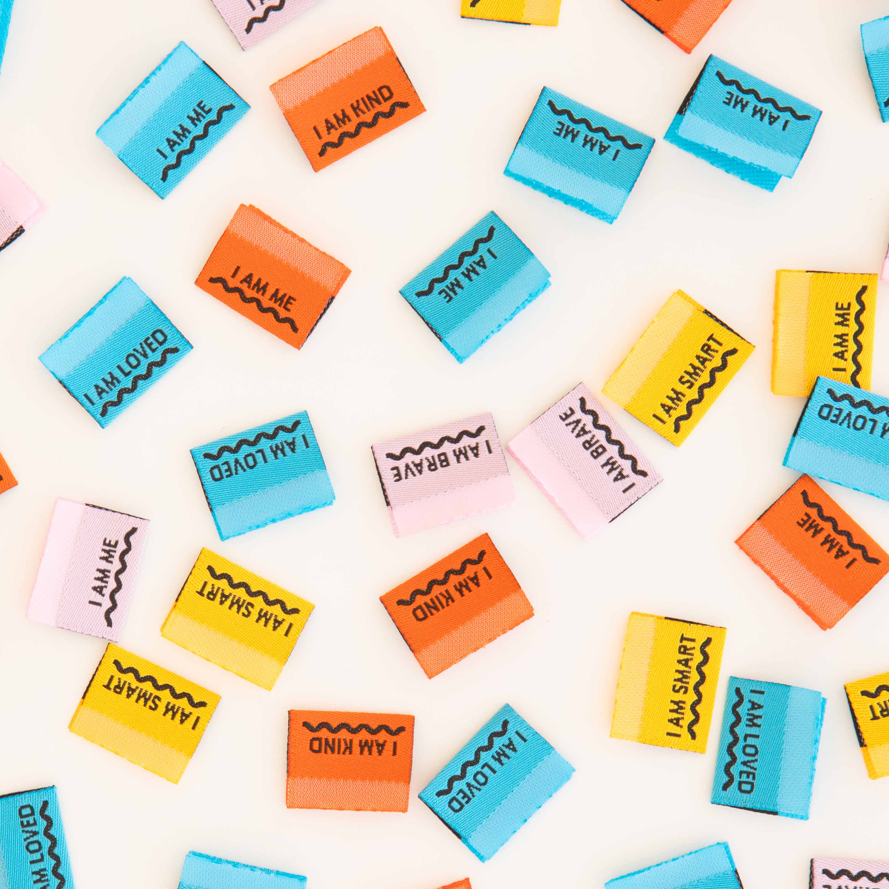 A colourful range of woven labels scattered across the table. All multicoloured and with different positive affirmations.