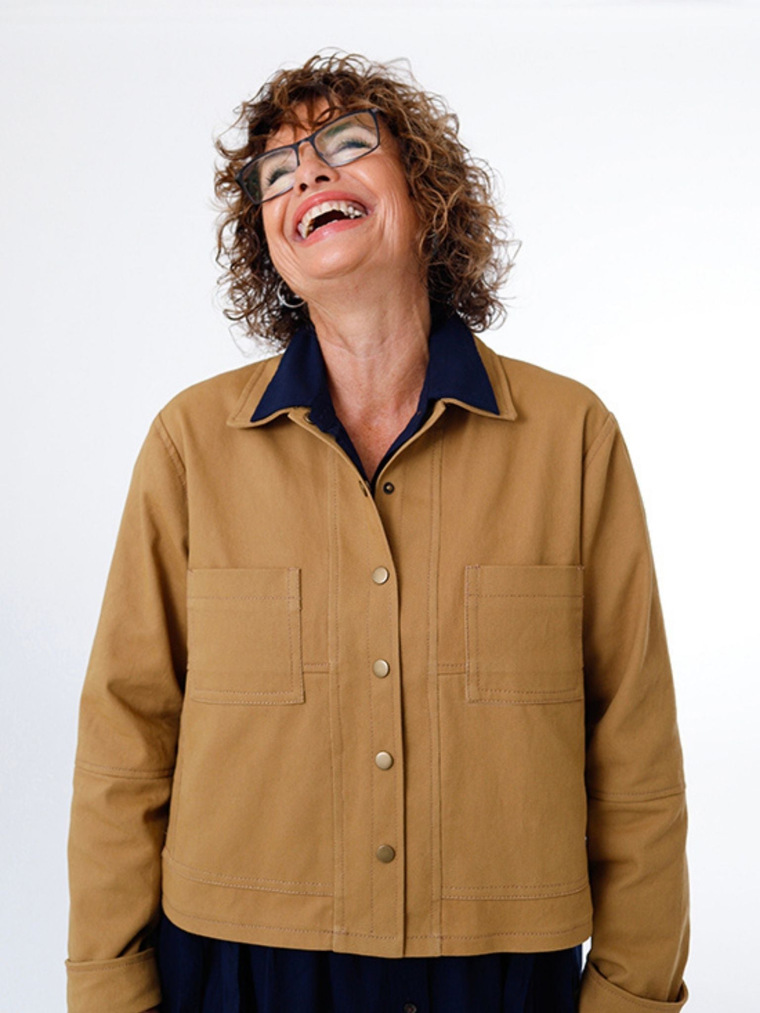 Smiling woman wearing a handmade tan button-up jacket with front patch pockets, made from the Carmen Jacket paper sewing pattern