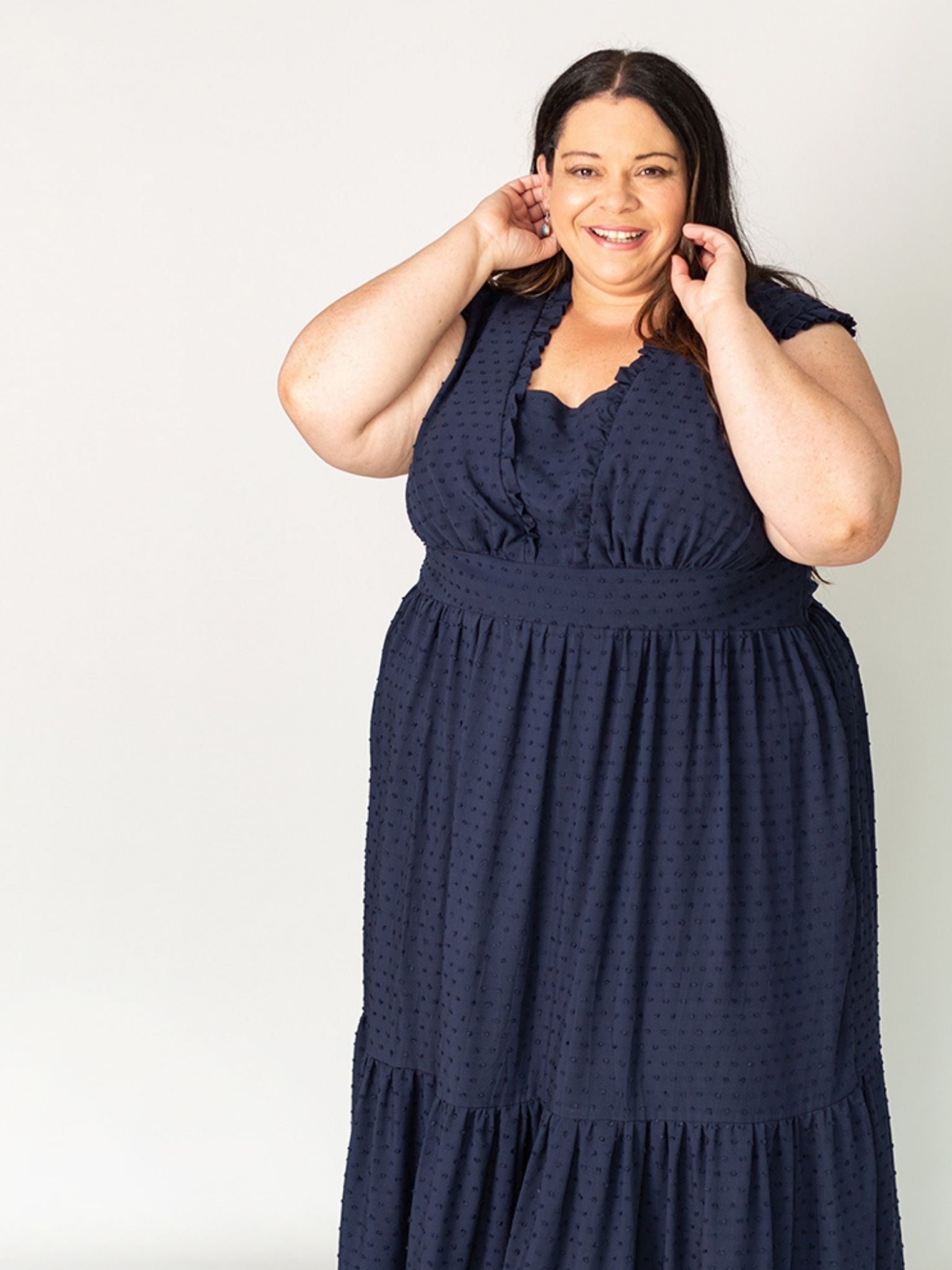Smiling woman wearing a handmade navy tiered maxi dress with ruffled neckline, showcasing a plus-size friendly sewing pattern design