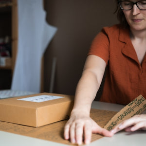 Rosie packing a sewing project kit box, folding kraft tissue paper to wrap the order
