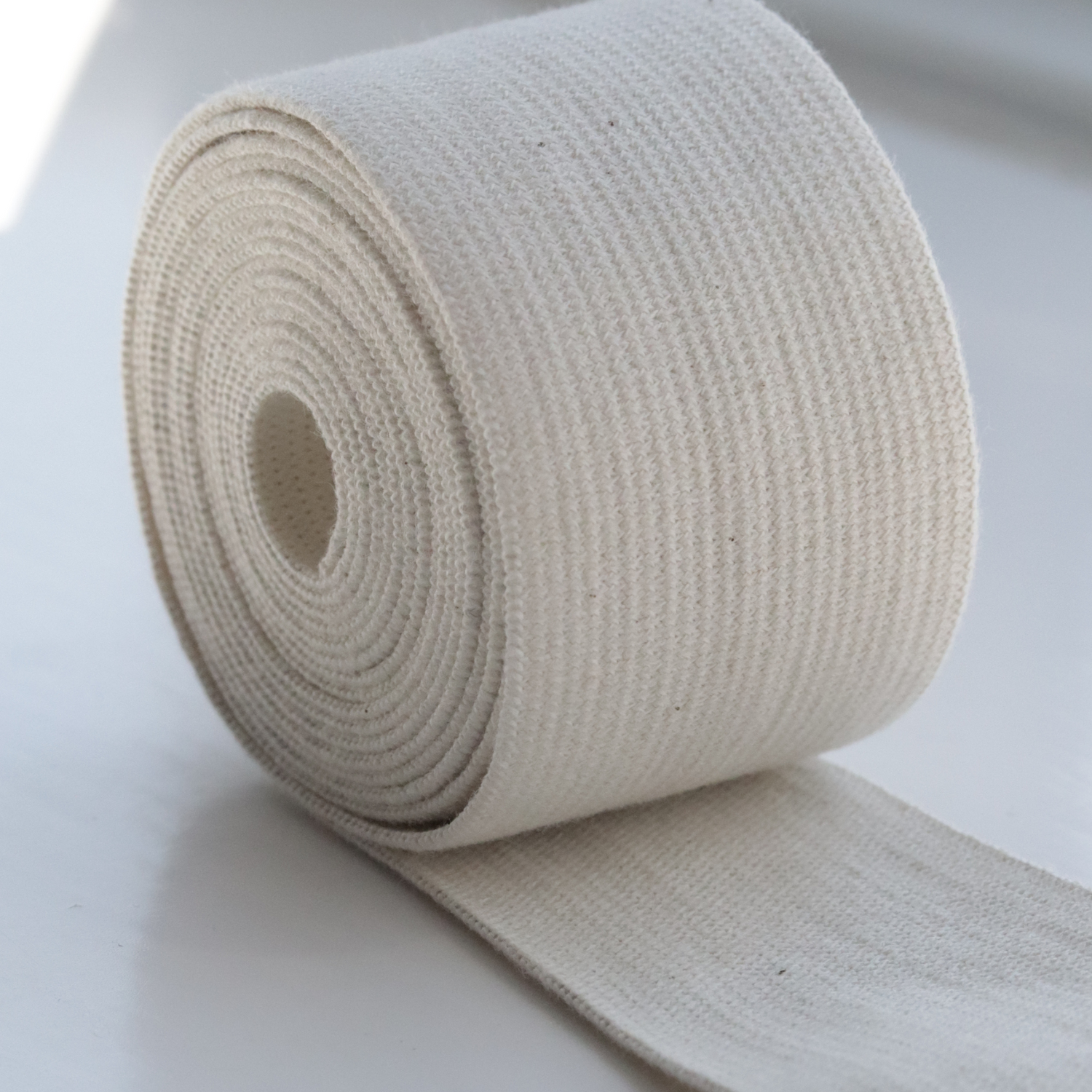 A roll of beige organic cotton elastic tape, partially unrolled, on a light background.