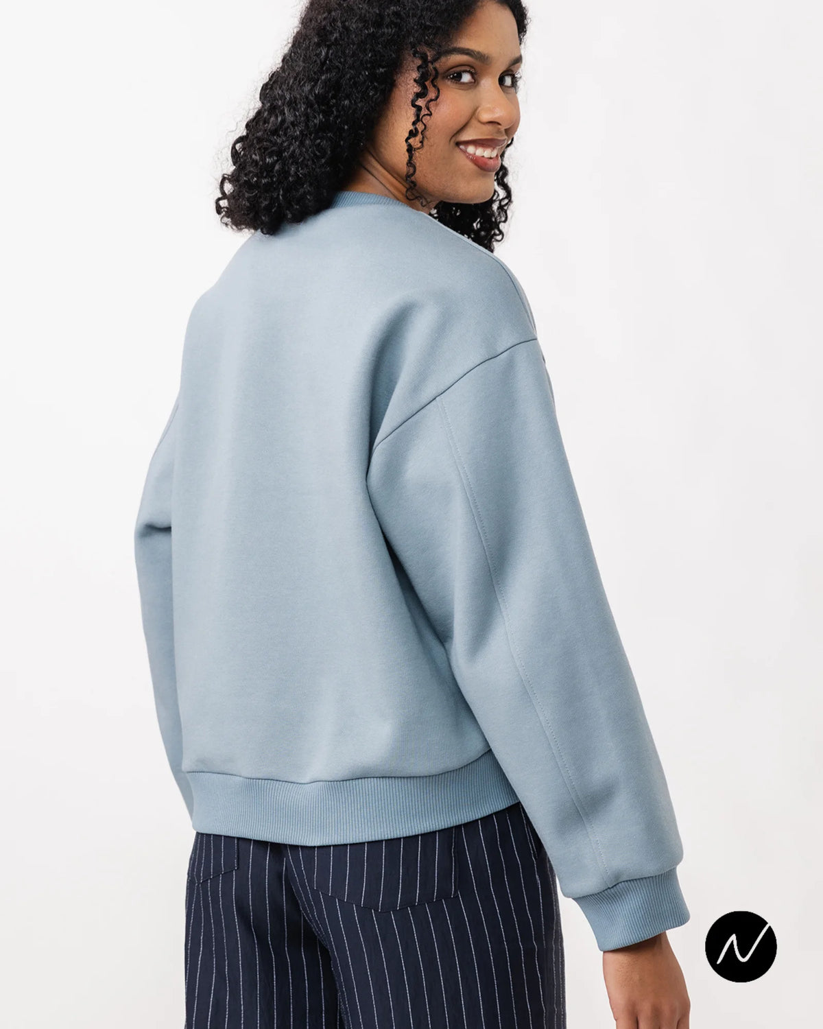 woman wearing a blue sweatshirt, showing the back of the jumper. A pdf sewing pattern from named clothing.