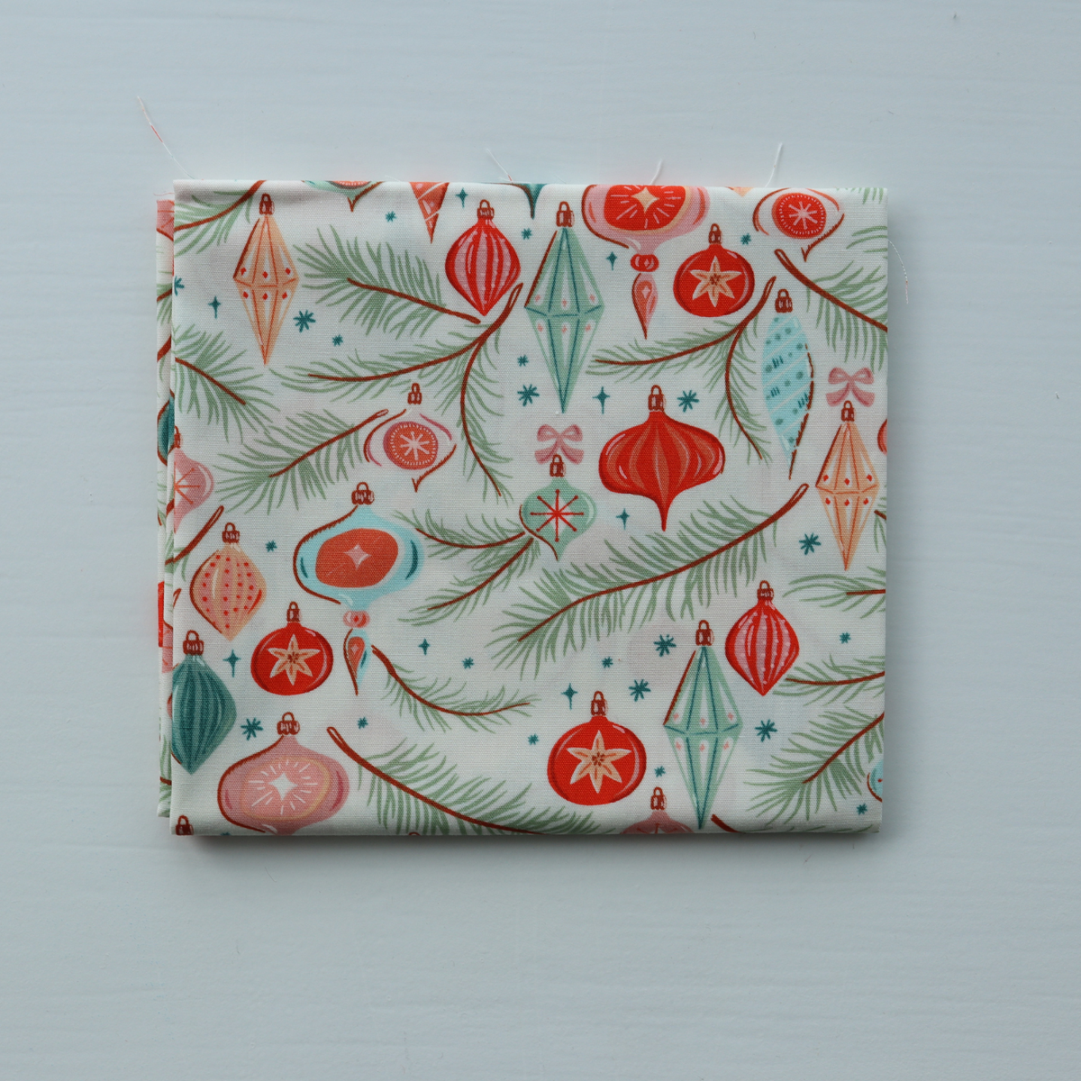 Fabric with Christmas-themed pattern featuring ornaments and trees on a light blue background