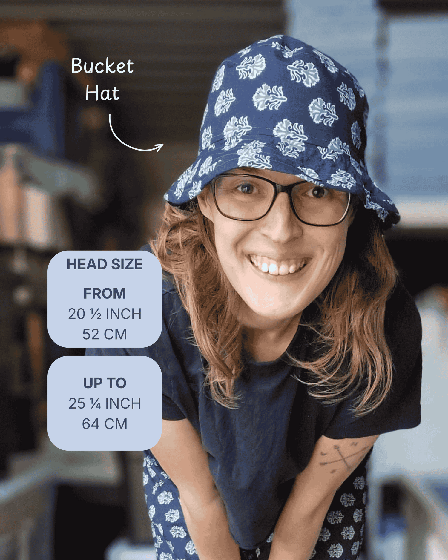 A woman wearing a navy blue bucket hat with a white floral pattern, shown in a lifestyle setting with text overlays detailing the head size range from 20 1/4 to 25 1/4 inches.