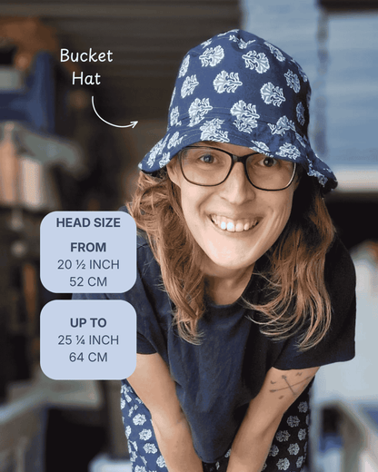 A woman wearing a navy blue bucket hat with a white floral pattern, shown in a lifestyle setting with text overlays detailing the head size range from 20 1/4 to 25 1/4 inches.