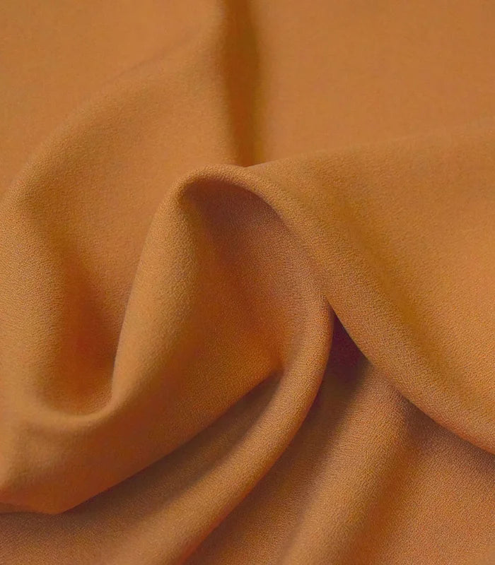 A close-up of draped fabric in a warm camel or tan color, showing soft folds and texture.