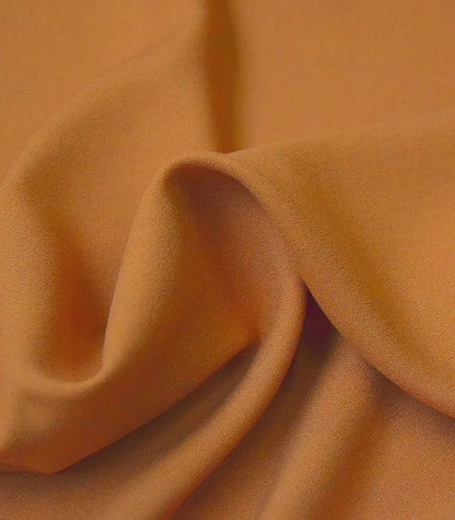 A close-up of draped fabric in a warm camel or tan color, showing soft folds and texture.