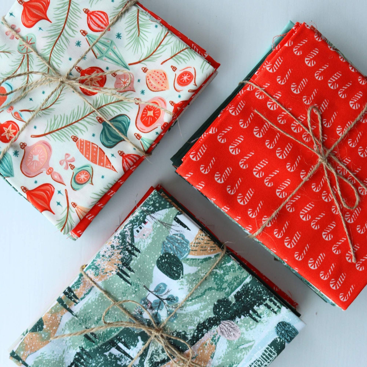Three wrapped fat quarter bundles with festive patterns on a white surface