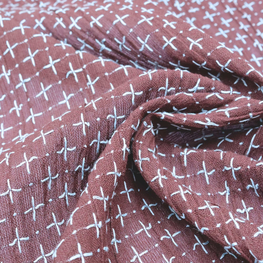 Close-up of a fabric with a pattern of white crosses on a maroon background