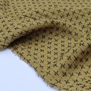 Close-up of mustard yellow cotton fabric with black cross stitch pattern, laying on a table