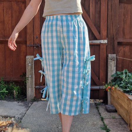 Person wearing blue and white gingham trousers with tie bow sides in front of a wooden fence.