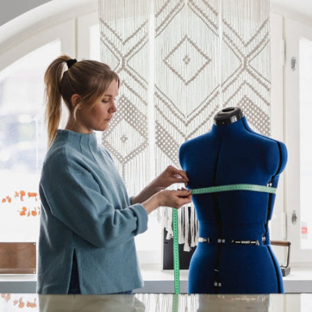 Person measuring a blue mannequin with a tape measure in a bright room.