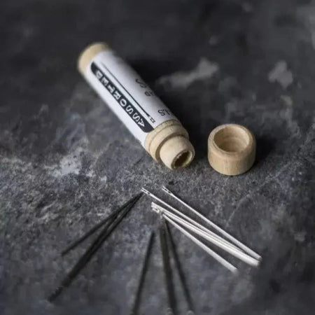 Set of metal needles with a wooden container on a dark surface
