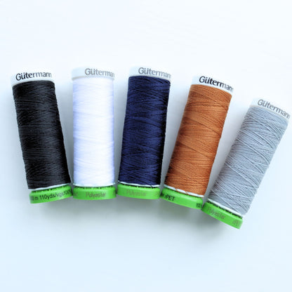 Five spools of Gutermann thread in black, white, blue, brown, and gray on a white background.