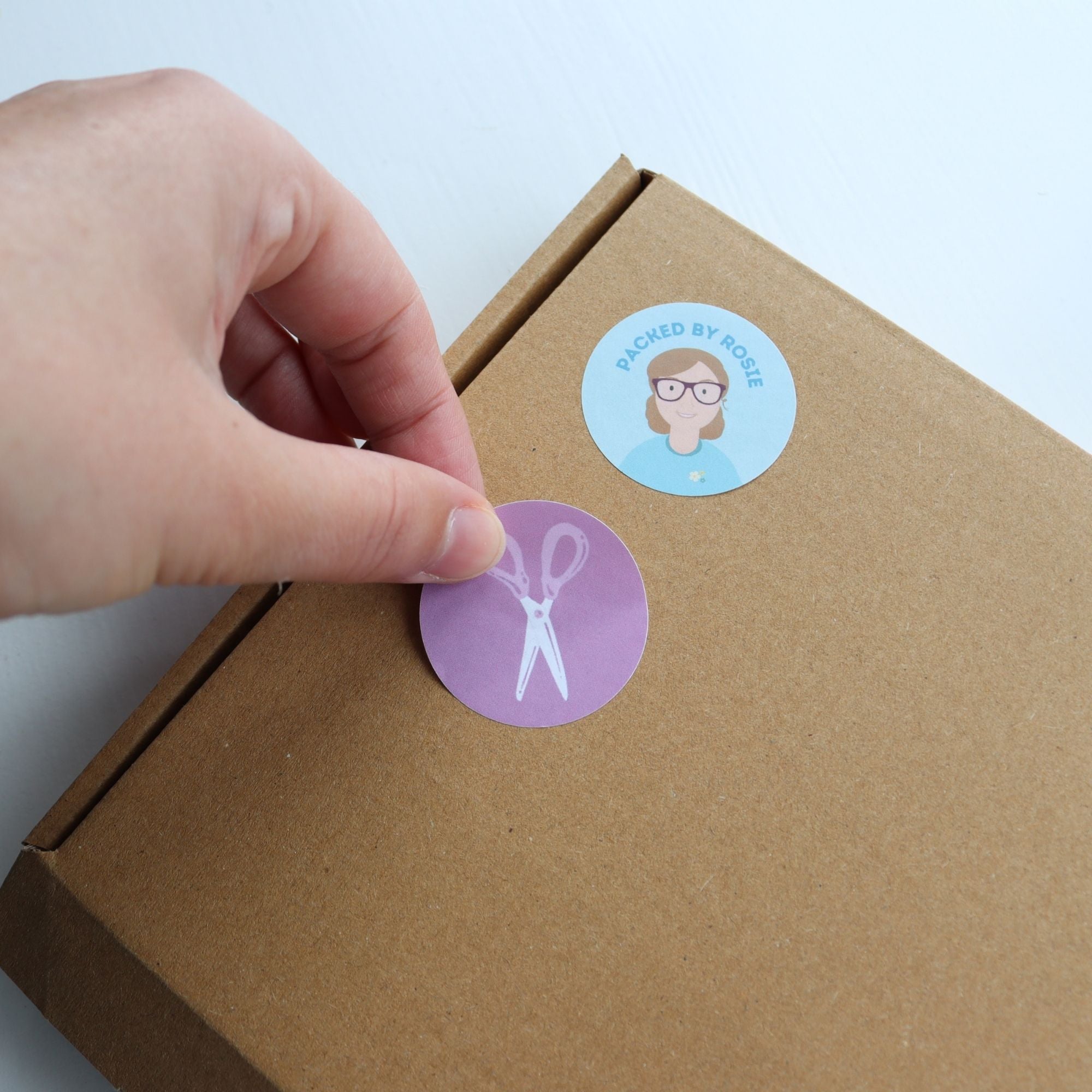 Hand placing a sticker on a cardboard box with another sticker already on it.