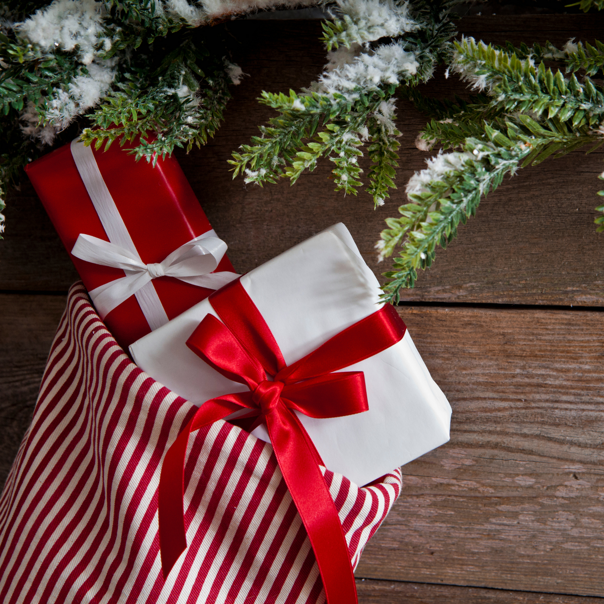 Two Christmas presents with red ribbons under a decorated tree on a wooden floor.