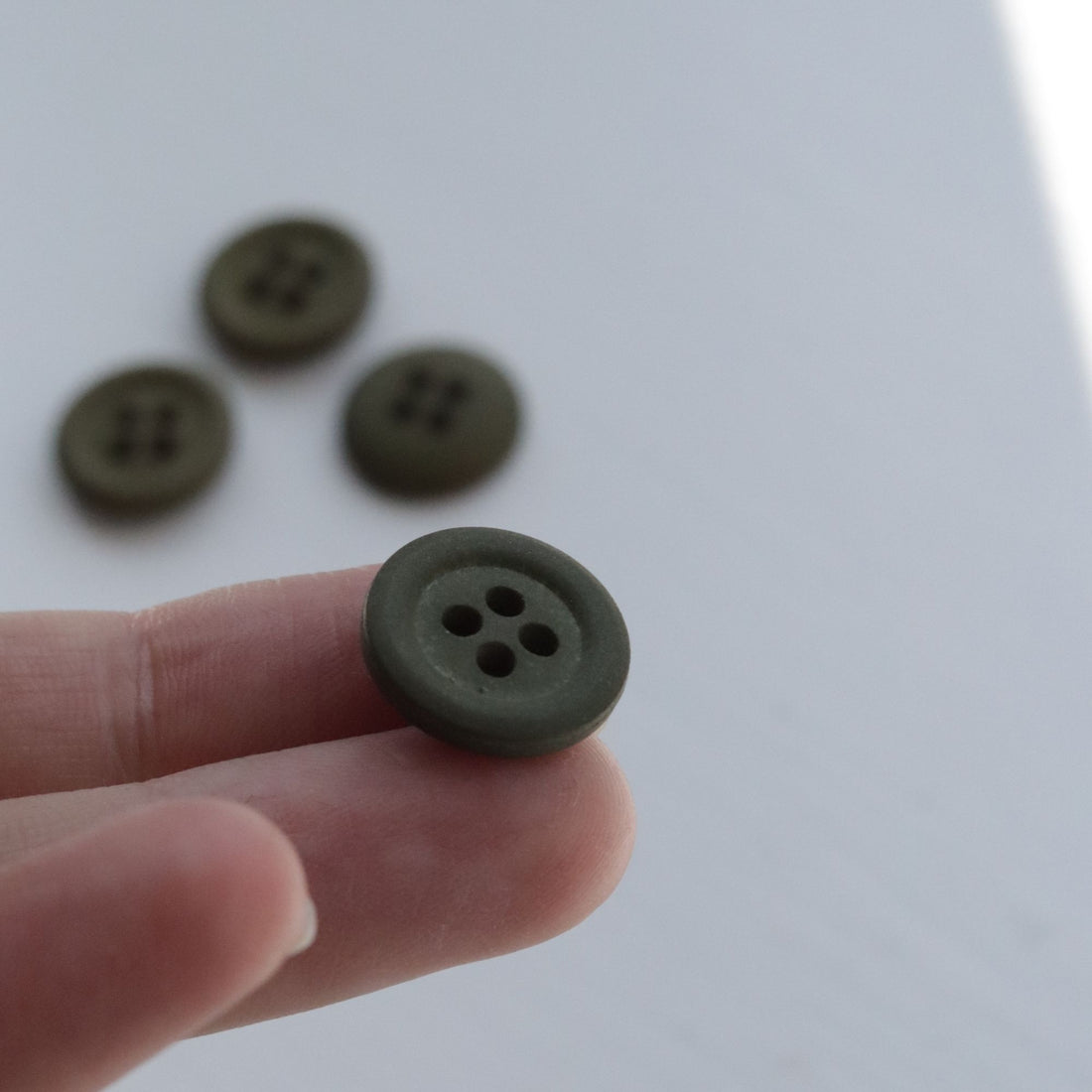 Hand holding a green button with other buttons in the background on a light surface.
