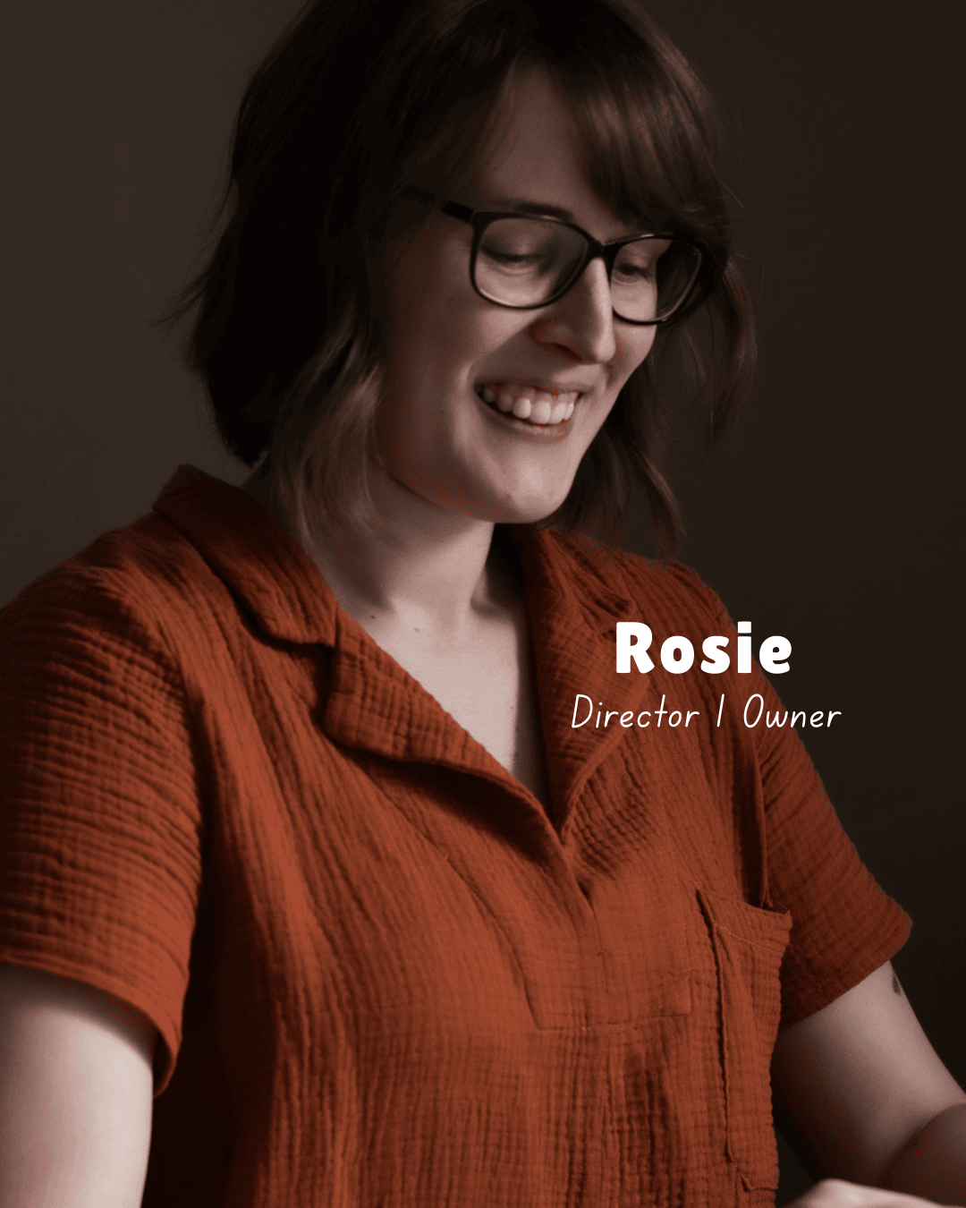 Woman wearing glasses and an orange shirt with 'Rosie Director Owner' text on a dark background