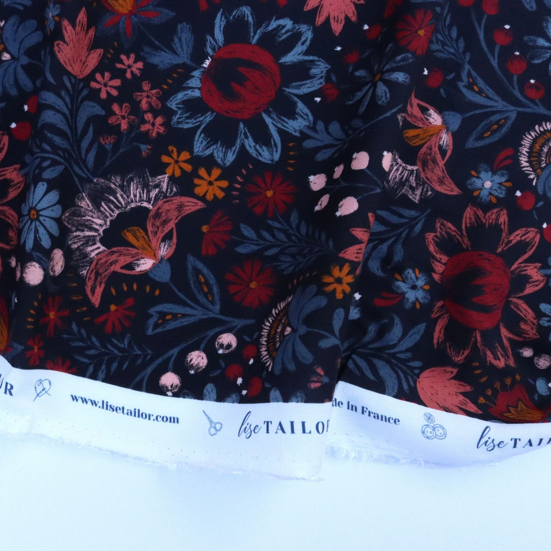 Floral fabric with red, blue, and pink flowers on a dark background, with Lise Tailor branding at the bottom.