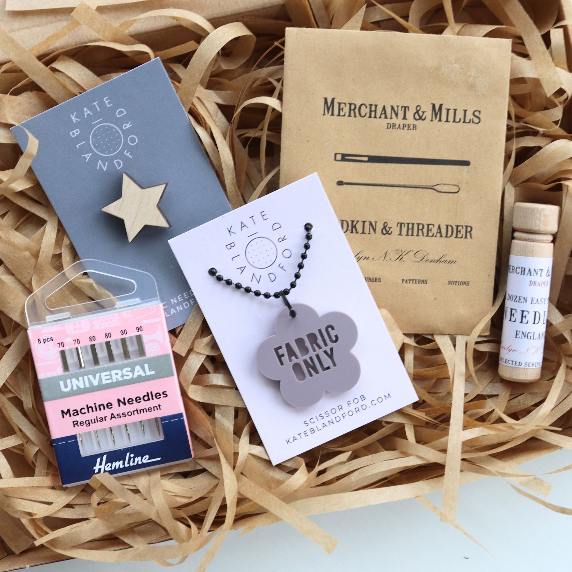 Collection of sewing supplies including a box, needle packet, and fabric tag on straw.