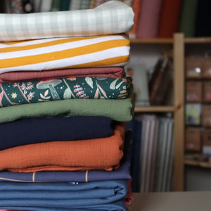 stack of folded fabrics, musty light blues, stripey yellows and forest designed greens flannels.
