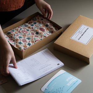 person packing a project kit with floral viscose fabric inside, adding the A0 pattern and thank you card