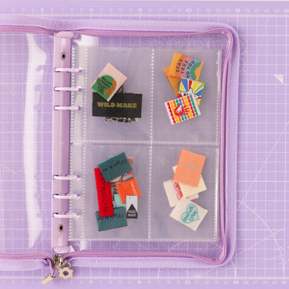 Clear Purple trimmed folder, with labels stashed inside the wallet. The folder is laying on a purple cutting mat. 
