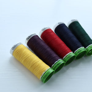 Five spools of Gutermann thread in yellow, purple, red, black, and green on a white background.