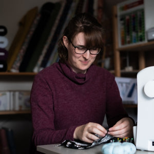 Person working on a sewing project at a table with a sewing machine.
