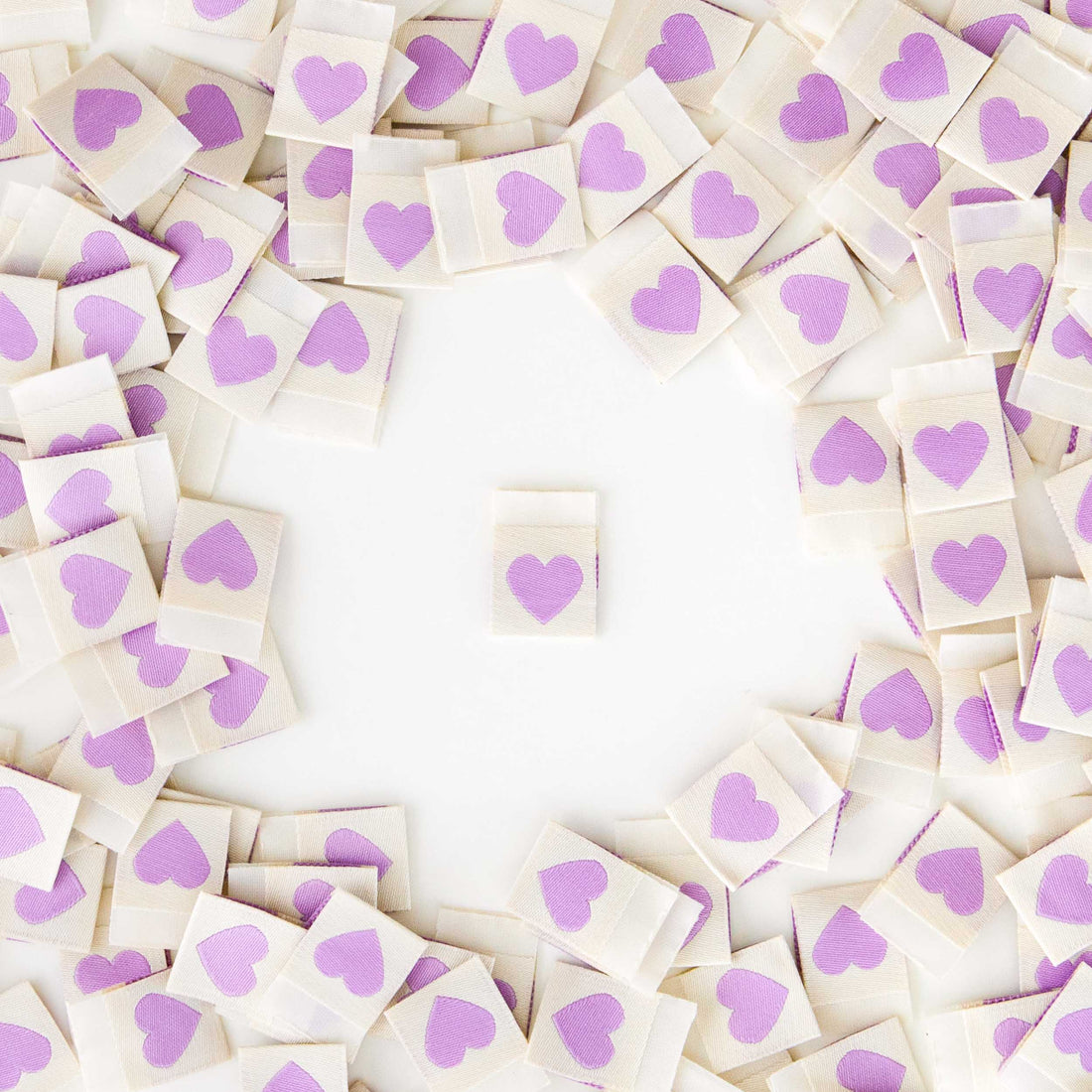 White Sew in Labels with light purple hearts. One Label sat in the middle, with a heap of labels around the edge.