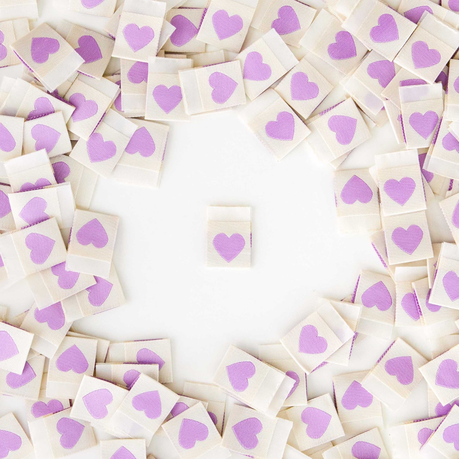 White Sew in Labels with light purple hearts. One Label sat in the middle, with a heap of labels around the edge.