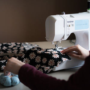 Woman using a Brother sewing machine sewing a floral fabric and reaching for a pin cushion