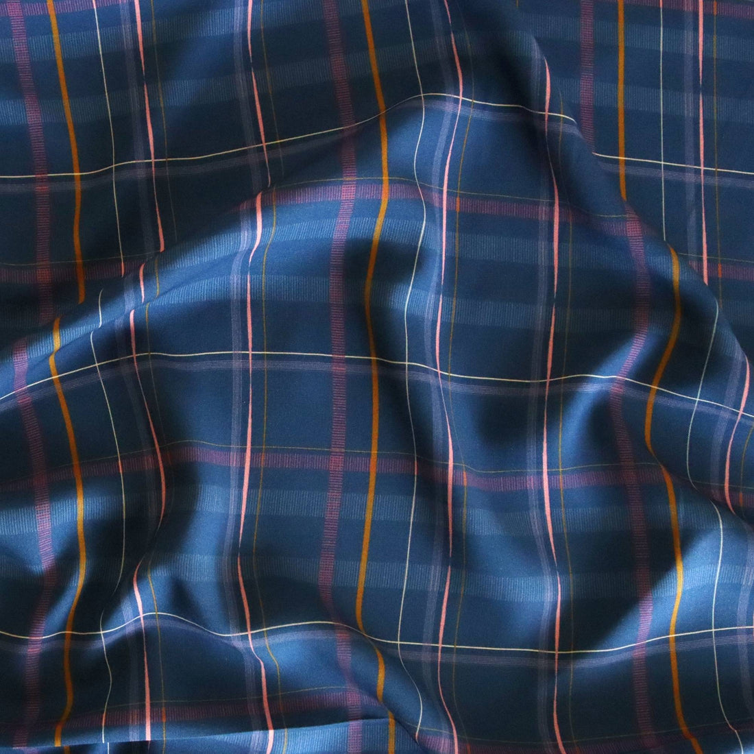 Deep navy viscose fabric with a bold check pattern in mustard, lilac, and rose pink lines, offering a structured yet drapey look for shirts, trousers, or dresses.