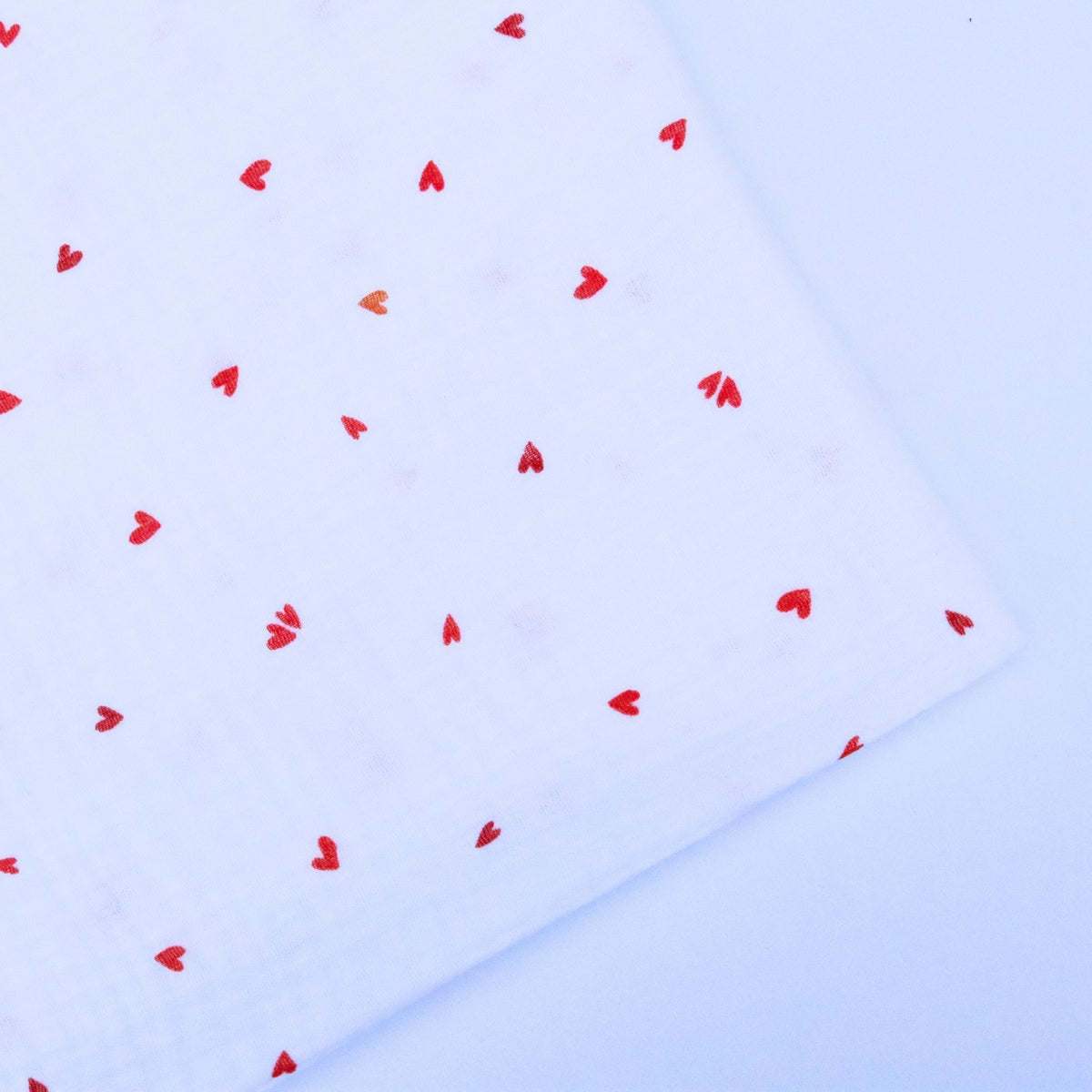 Red heart shapes scattered on a white double gauze cotton on a light background