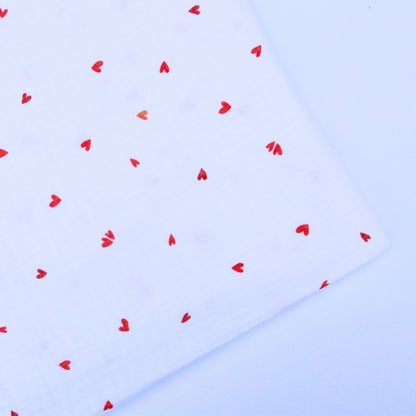 Red heart shapes scattered on a white double gauze cotton on a light background