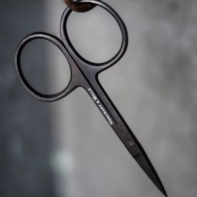 Pair of black scissors hanging on a rusty hook against a gray background
