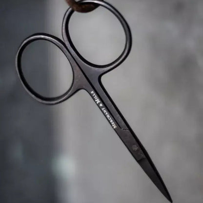 Pair of black scissors hanging on a rusty hook against a gray background