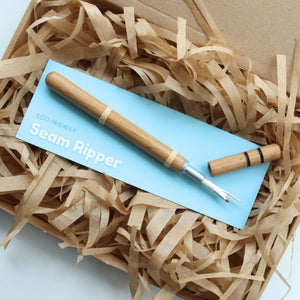 Seam ripper on a blue card with a brand name, placed on shredded paper.