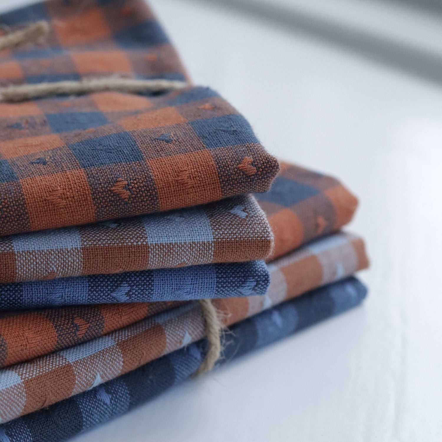 Close-up of folded Fableism fat quarters in rust and blue gingham, stacked neatly to show texture and woven heart details.