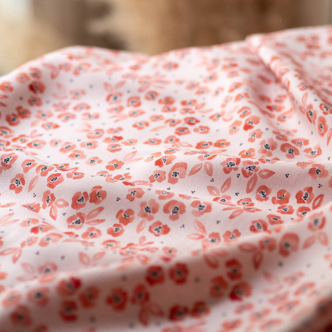 Softly draped Feline Floral viscose fabric in natural light, showing coral floral clusters on a blush pink background with pampas grass blurred in the background