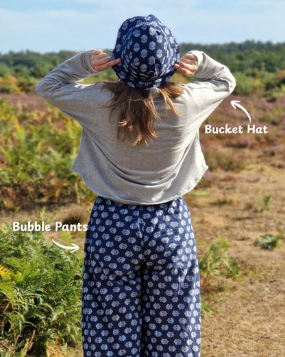woman wearing blue block print trousers and bucket hat, walking along in nature