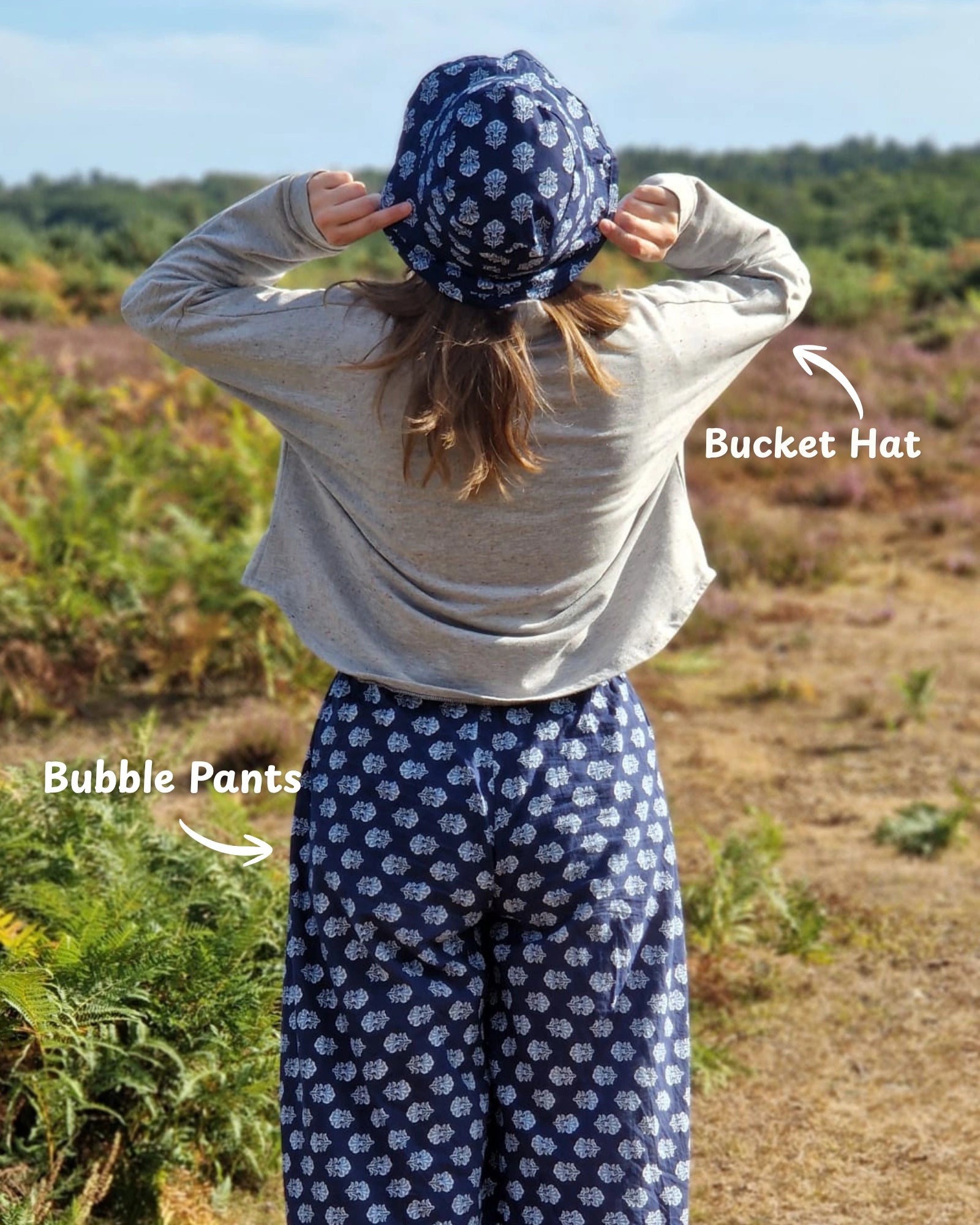 woman wearing blue block print trousers and bucket hat, walking along in nature