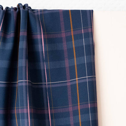 Silhouette viscose fabric hanging in soft folds, showing navy base with mustard and pink plaid lines.