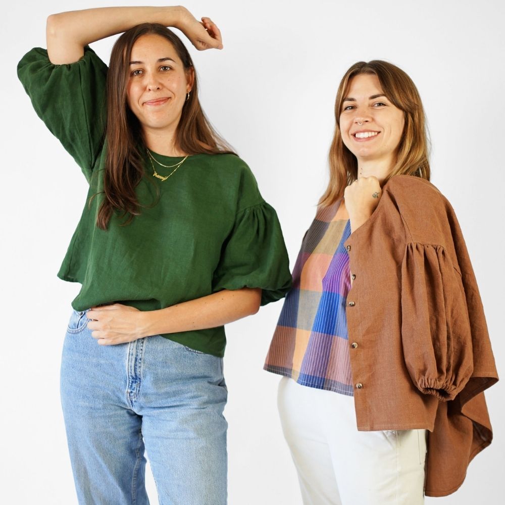 Two women wearing handmade garments—one in a green puff-sleeve blouse, the other in a colourful top with a brown buttoned jacket—made from modern PDF sewing patterns