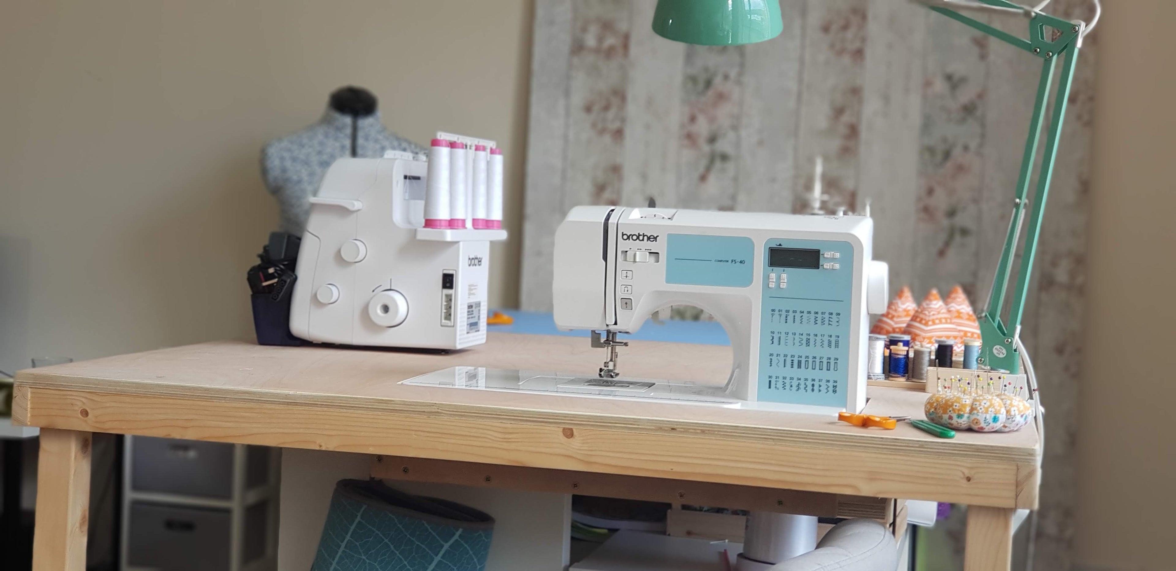 Sewing machine integrated into a standing sewing table. Aside the sewing machine is a pin cushion, pattern weights and an over locker machine.